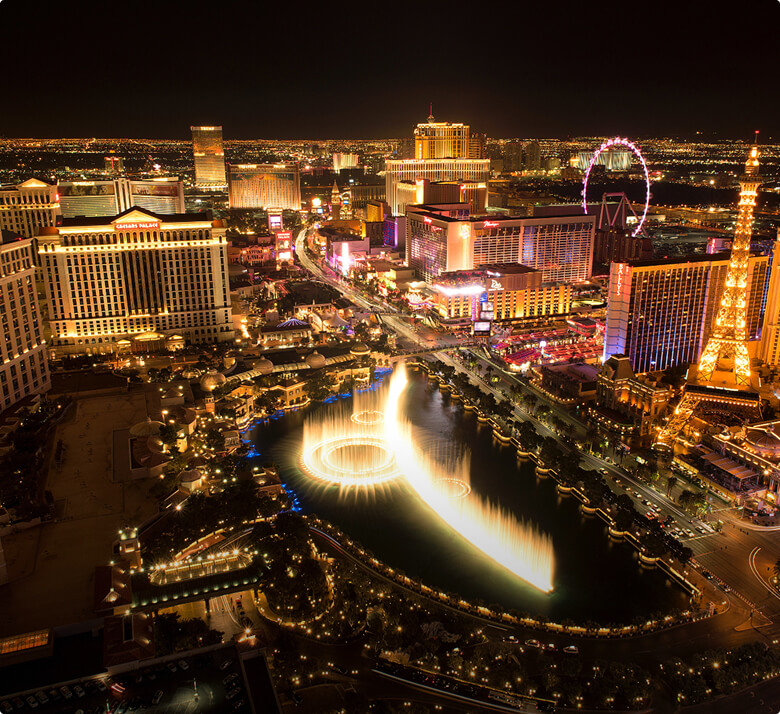 A nighttime skyline of Las Vegas featuring a water fountain. The image represents {{50+ Years Serving the Las Vegas Community}}